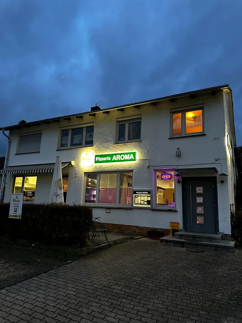 Außenansicht von Pizzeria Aroma am Abend mit beleuchtetem Schild