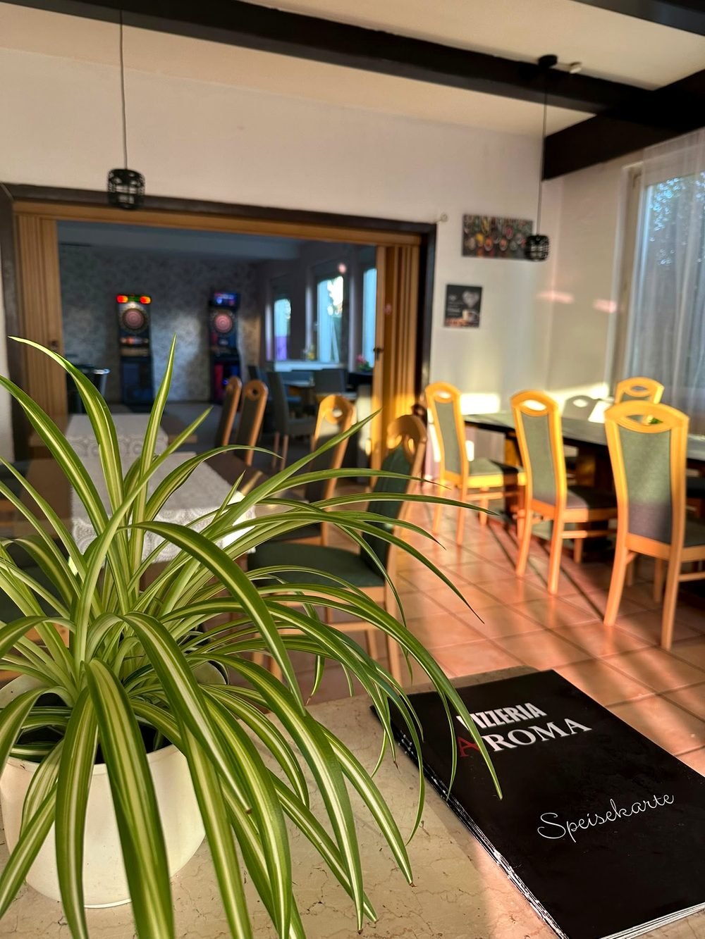 Gemütlicher, heller Gastraum von Pizzeria Aroma mit Tischen und Zimmerpflanze